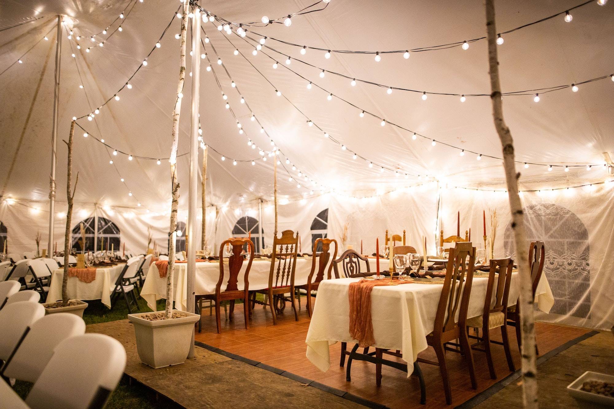 Wedding venue tent with dinner equipment on tables and string lights